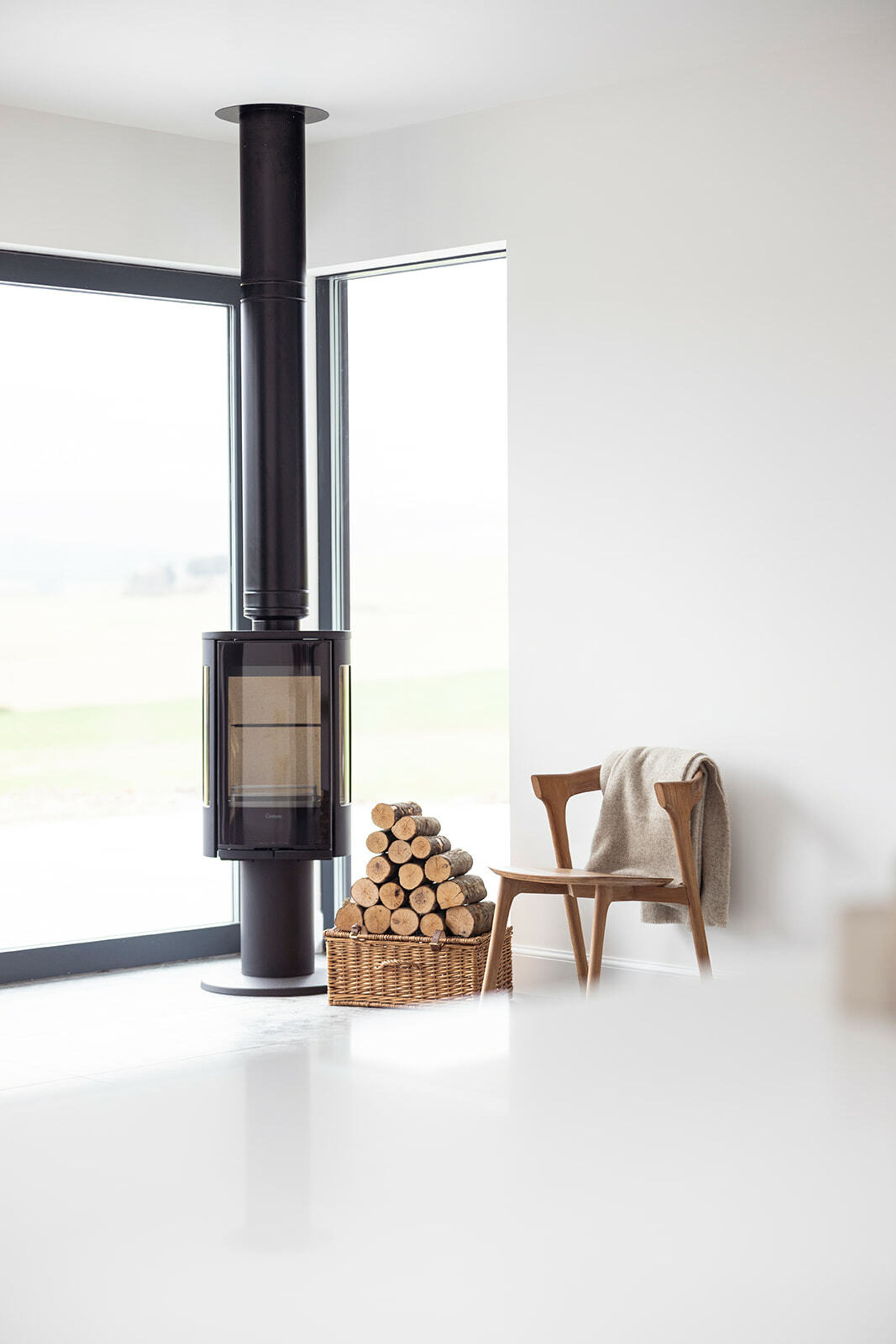 A black woodburning stove. Logs sit on a basket next to the stove. A chair sits next to the basket with a throw draped over it.