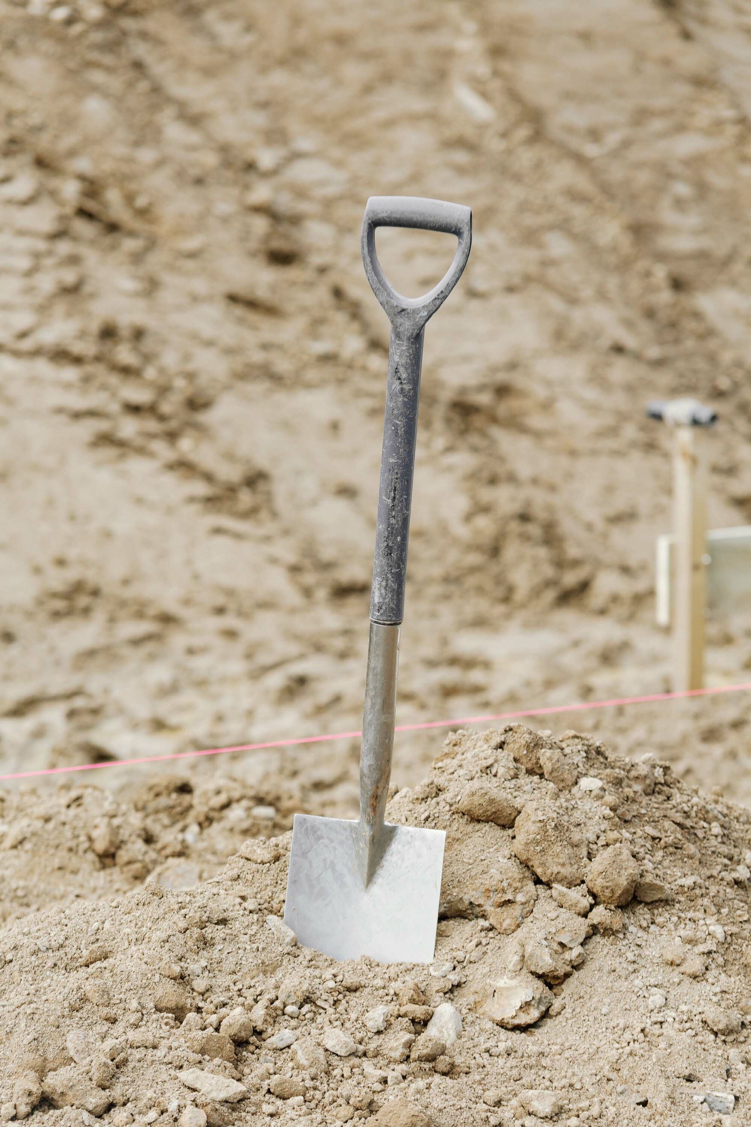 A shovel stuck into a pile of earth. Pink builder’s line is stretched out the background.