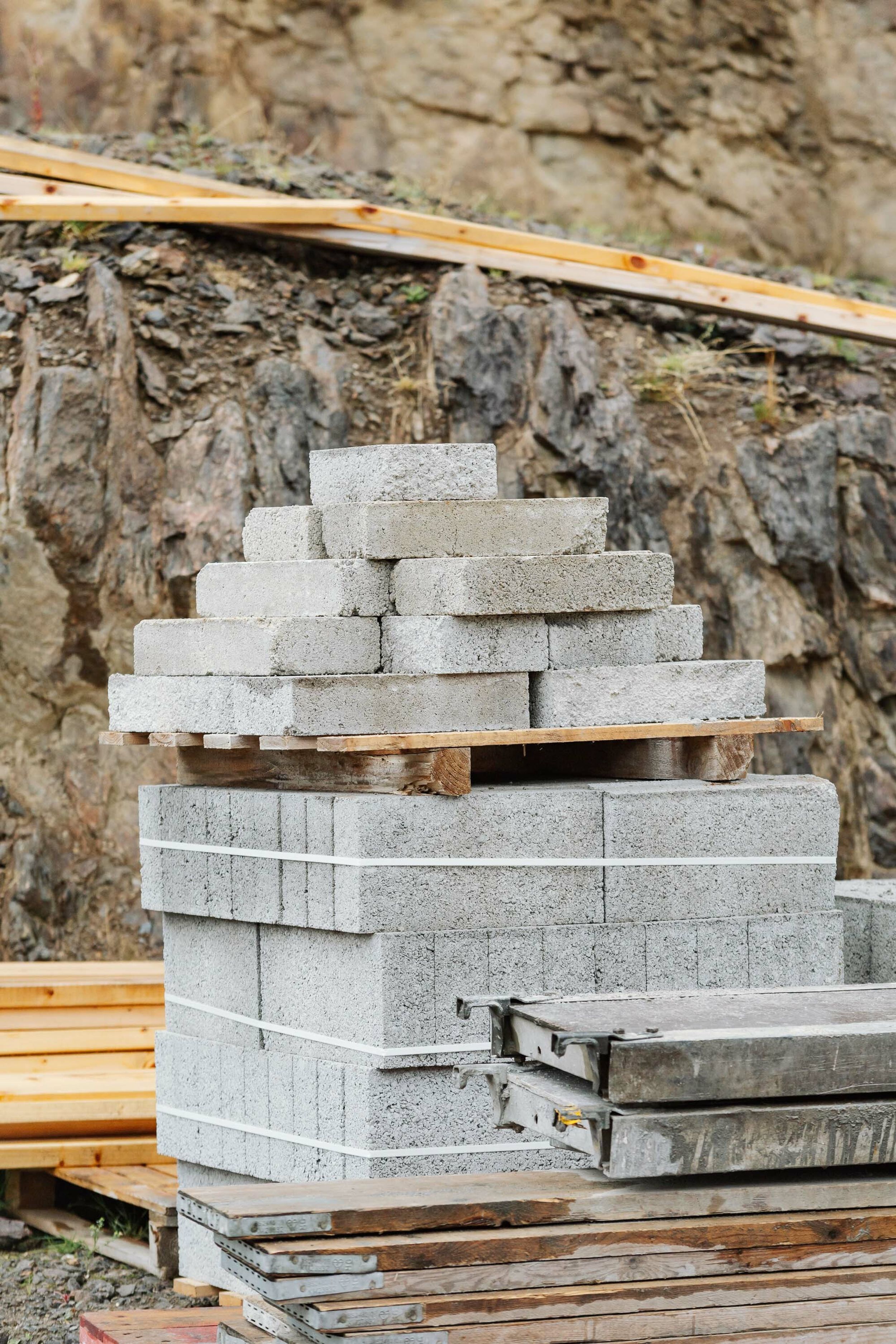 Concrete blocks and scaffolding boards stacked on a building site. Exposed rock is in the background.