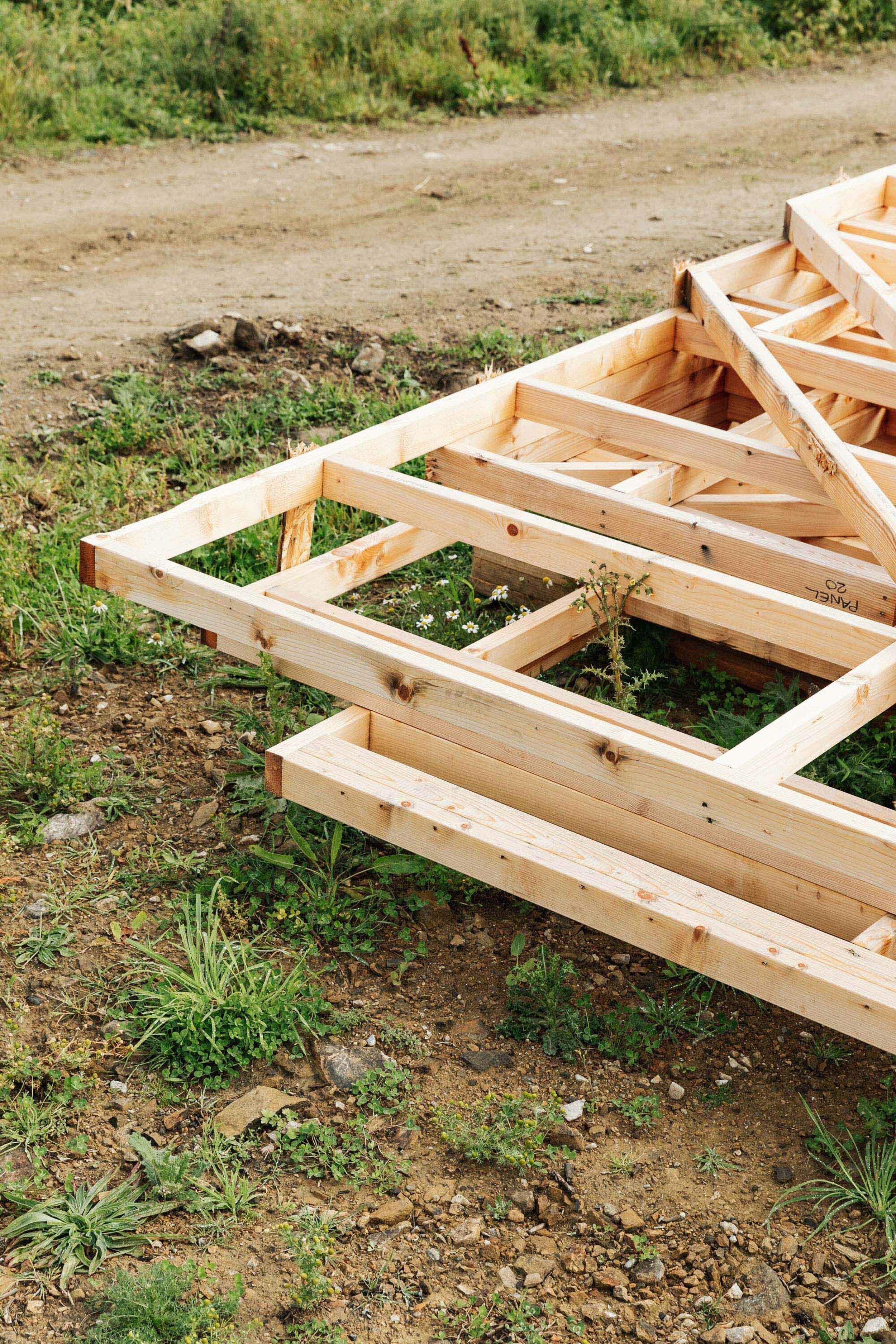A timber frame sits on the ground at a new build construction site. Grass and daises surround the timber.