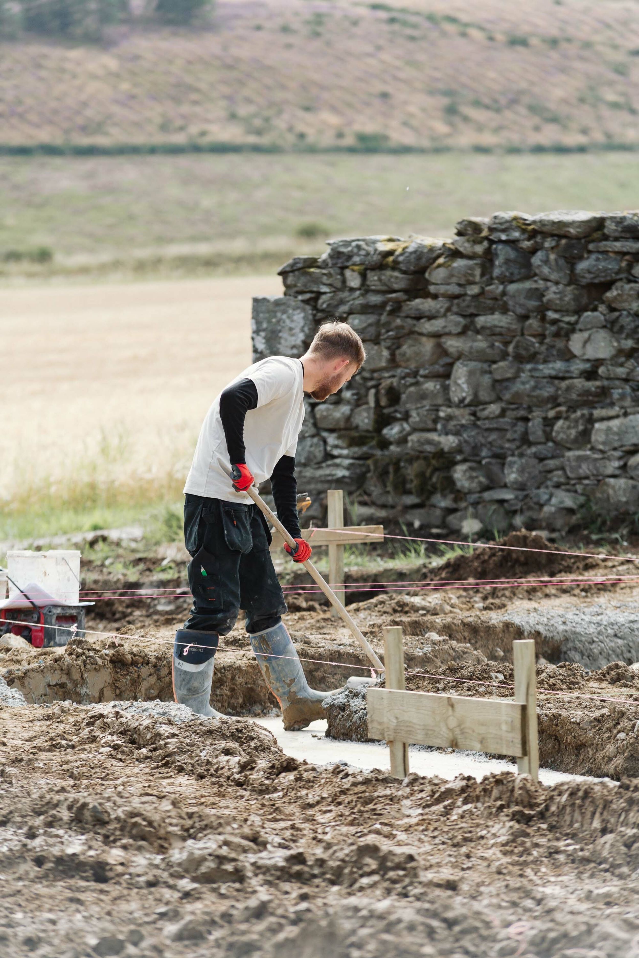 A builder uses a broom to sweep the mud from the concrete foundations of a new home.