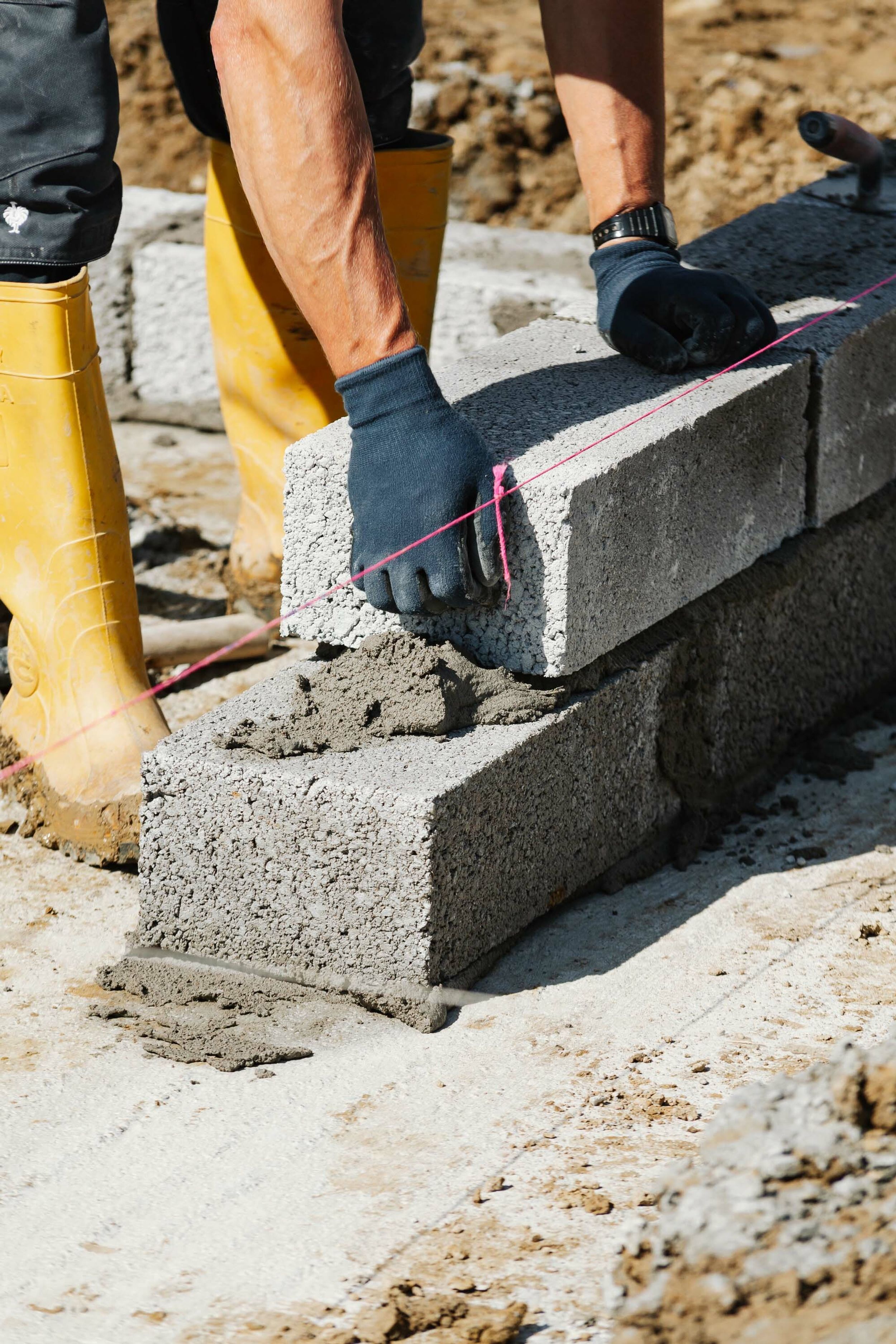 A construction worker lays concrete blocks in wet cement to build the finished floor height of a new build home.