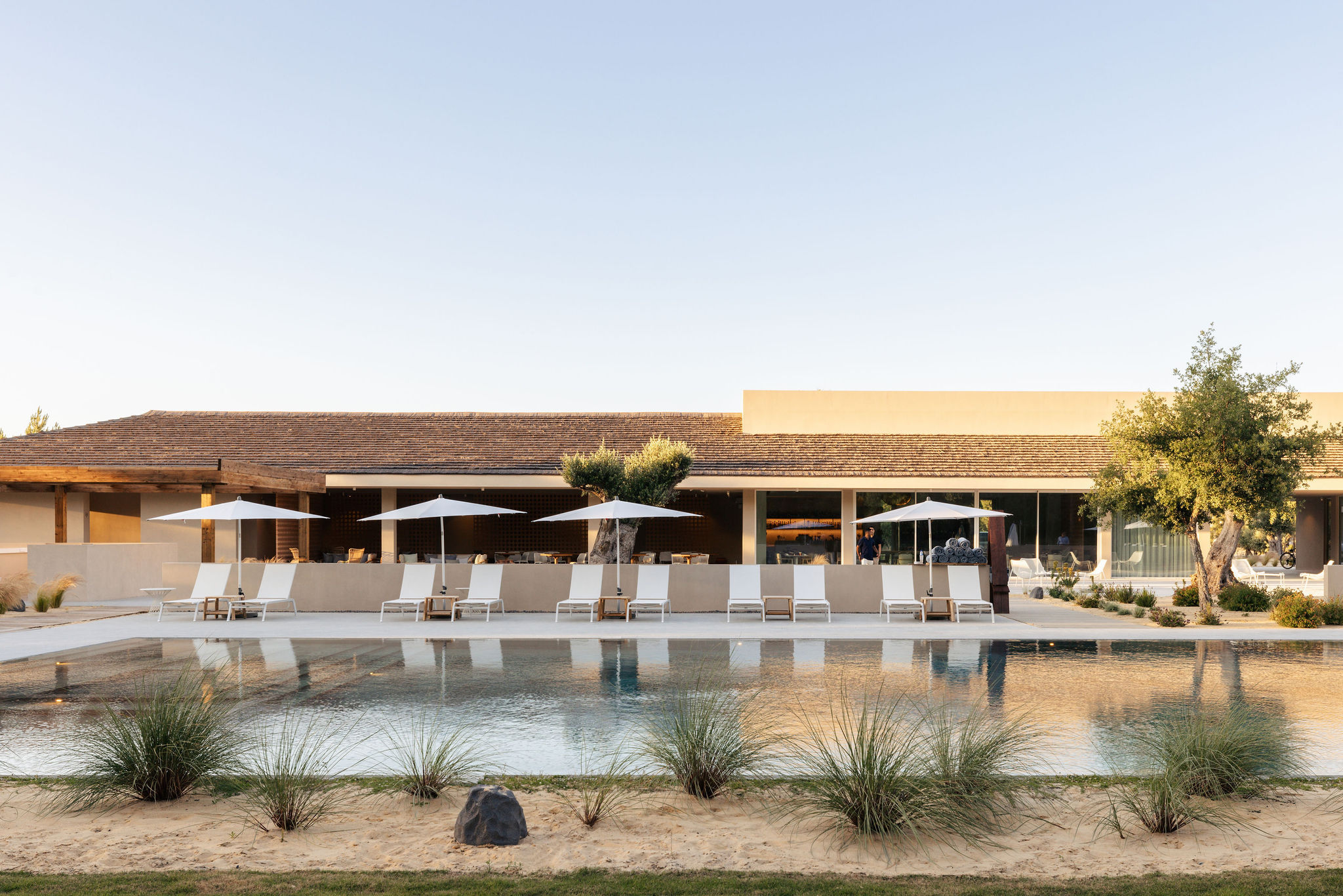 Spatia Comporta clubhouse and pool at golden hour, umbrella pines beyond