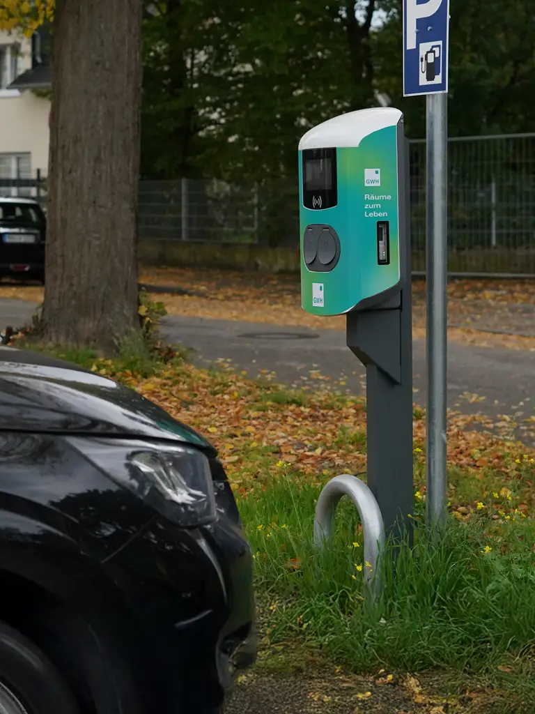 Ladestation für Elektroautos an einem Straßenrand mit geparktem schwarzem Auto im Vordergrund