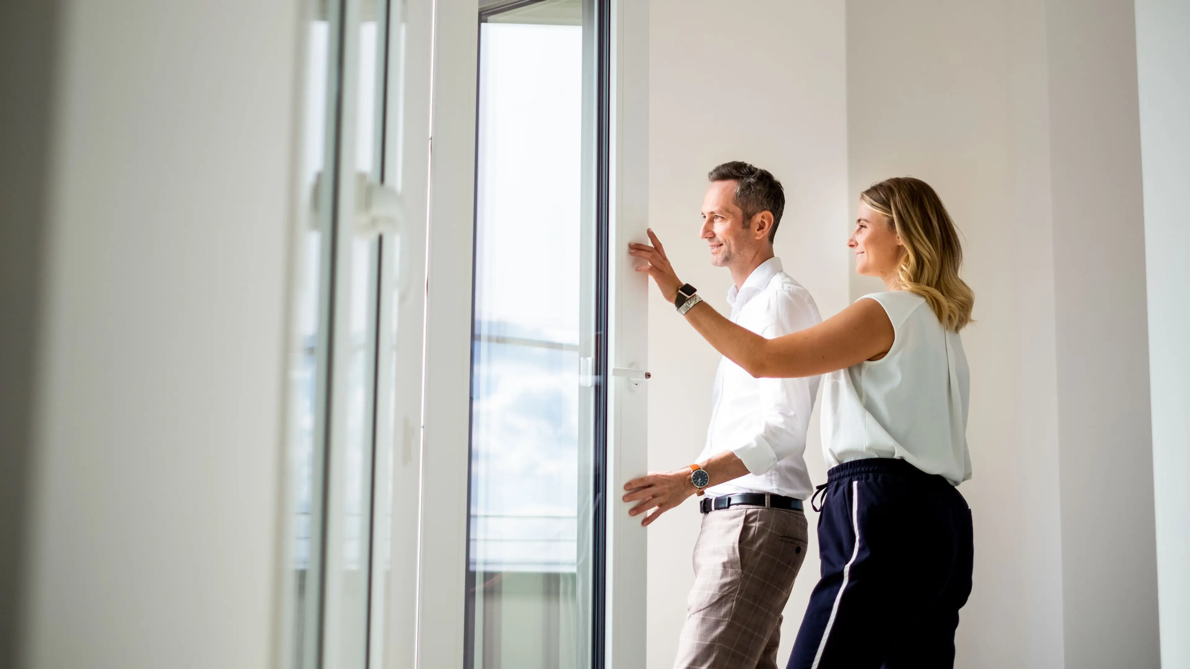 Mann und Frau stehen in ihrer neuen Wohnung und schauen aus dem Fenster