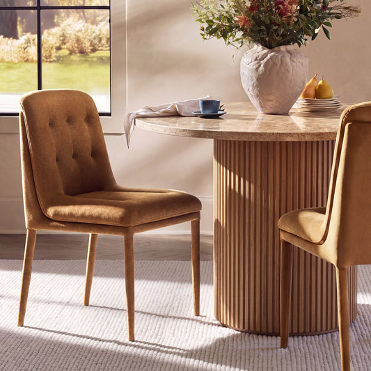 Two brown upholstered chairs flank a round veined table with a vertically ribbed pedestal