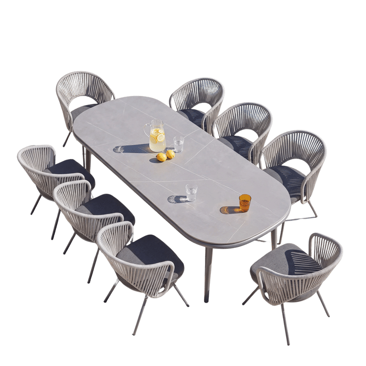 Long gray oval dining table surrounded by woven gray dining chairs on a black background