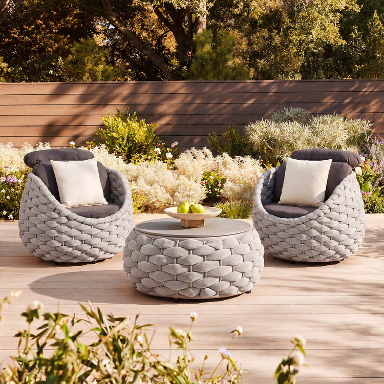 Two woven lounge chairs flank a round matching table, Gray seating stands on a sunny garden deck