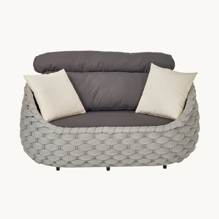 A gray woven loveseat appears frontally with dark cushions, Two cream throw pillows rest against the back