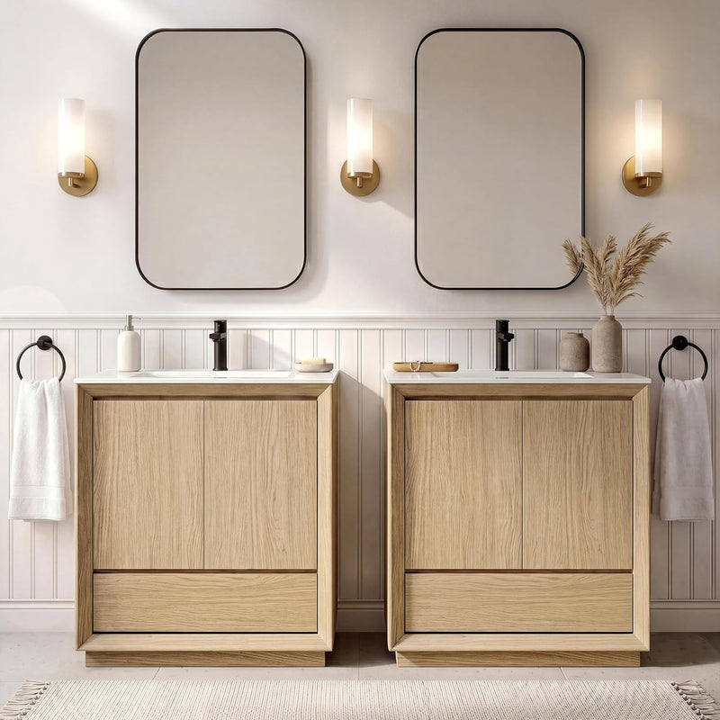 Two light wood-grain vanity cabinets have white sinks and black faucets, Rounded mirrors and three lit wall sconces hang above