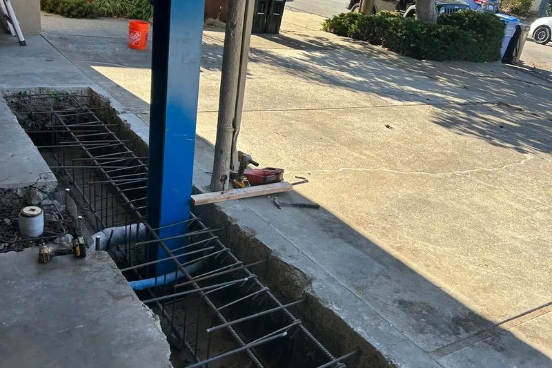 Steel column and reinforcing rebar in an excavated foundation trench beside a driveway