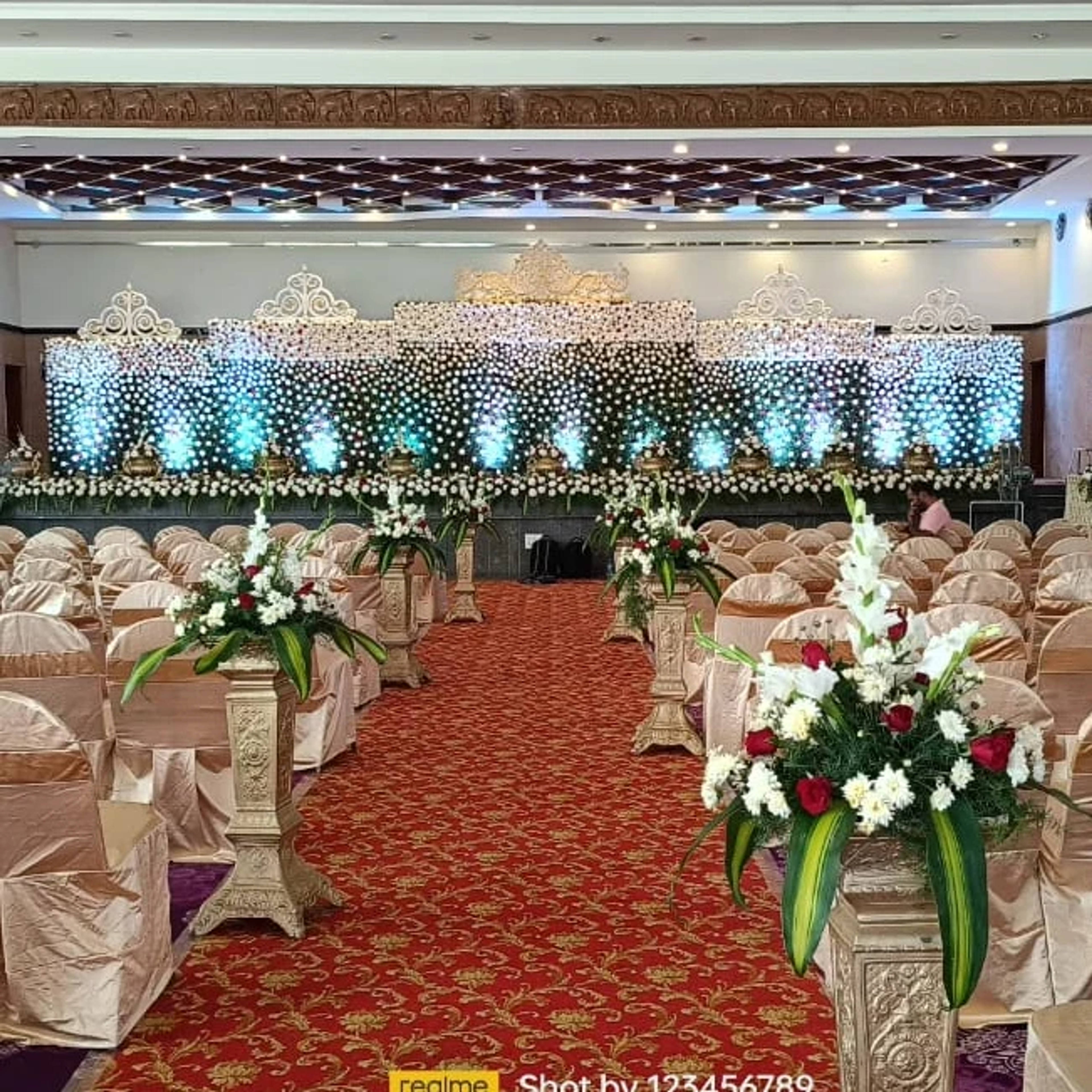 Pearl-curtain stage with blue uplight and flower stands along the aisle