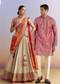 Festive Wedding Couple Set – Orange Brocade Bridesmaid Lehenga with Leheriya Dupatta for Her And Pink Embellished Tissue Kurta Set for Him