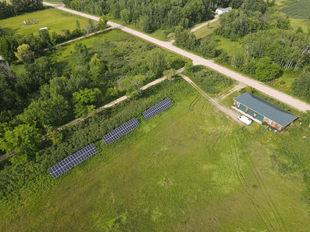 Drone view of ground mounted solar arrays and Rusty Shed with three oversize garage doors.