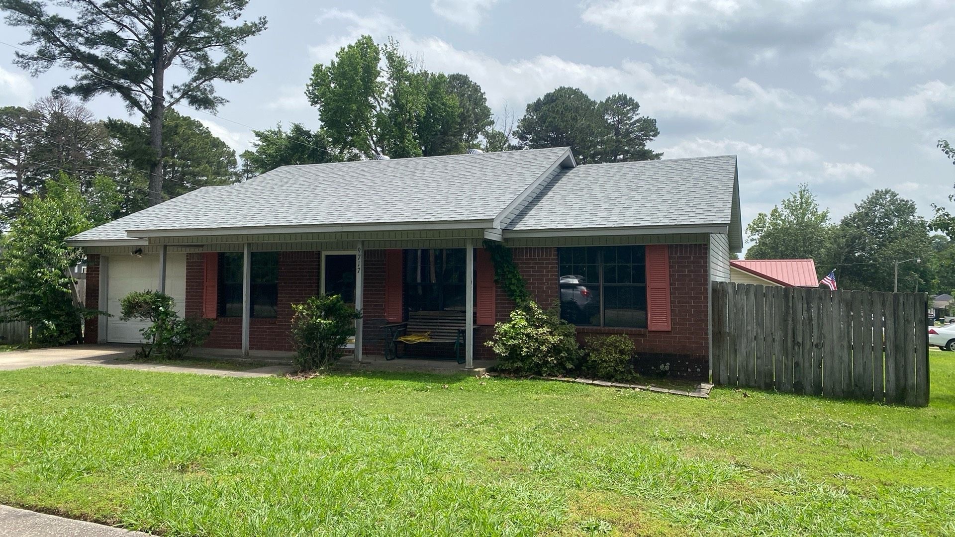 Single-story brick house with a front porch, lush green lawn, and trees nearby.