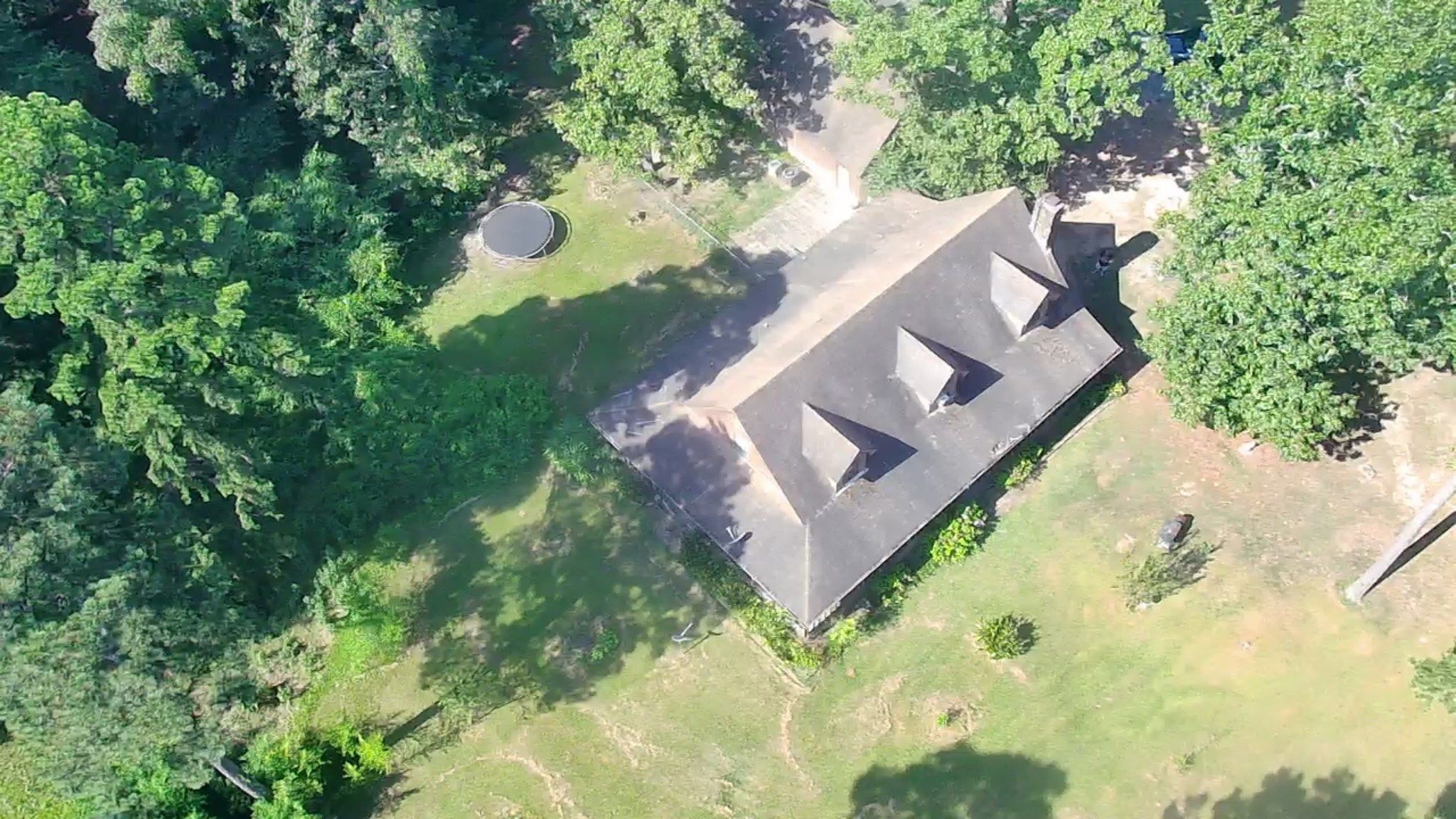 Aerial view of a large house with triangular roofs surrounded by green trees and grass.