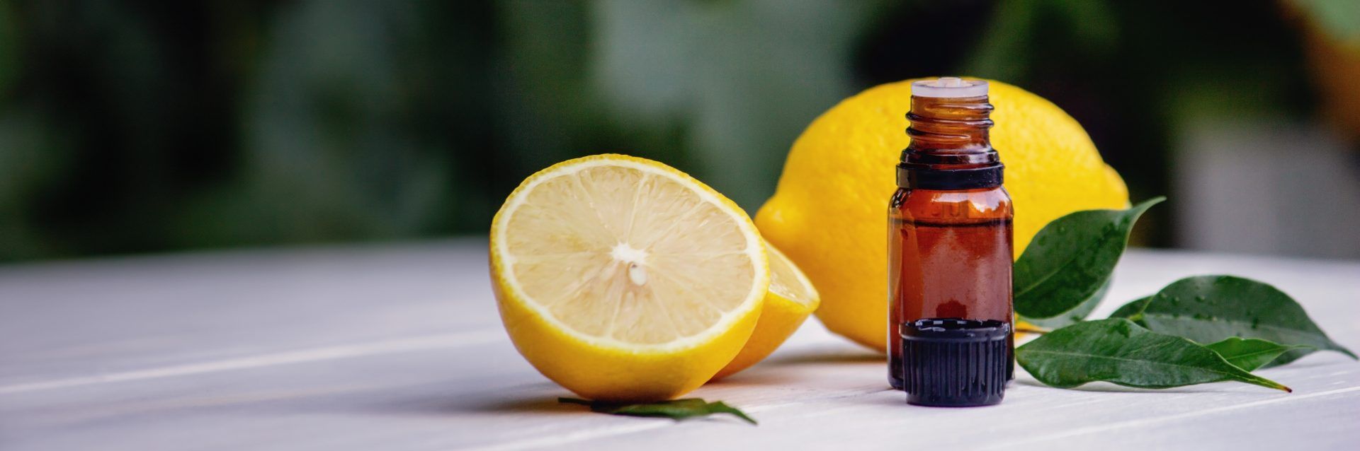 Lemons, one cut and one uncut, sit next to an open bottle of oil and a sprig of thyme