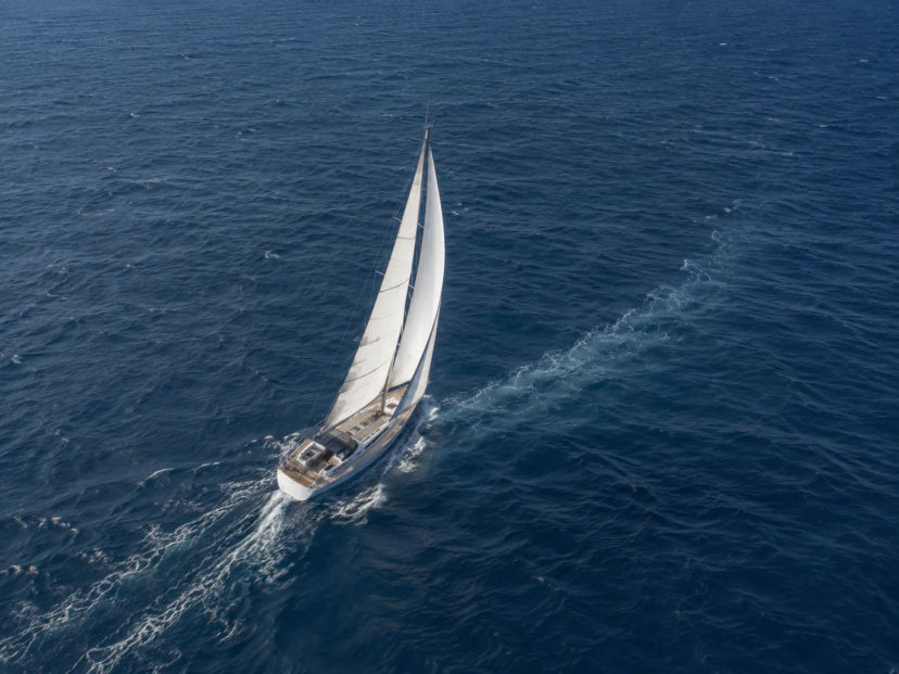 White sailboat heeling under full sail with a white wake on deep blue open sea