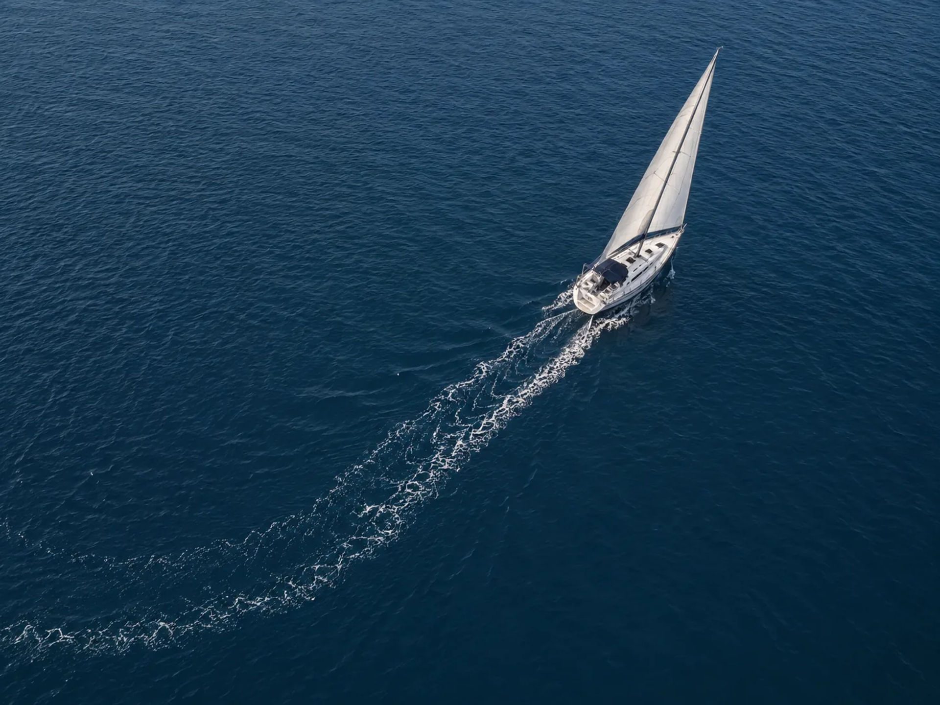 Aerial view of a white sailboat with sails deployed leaving a long wake on the ocean