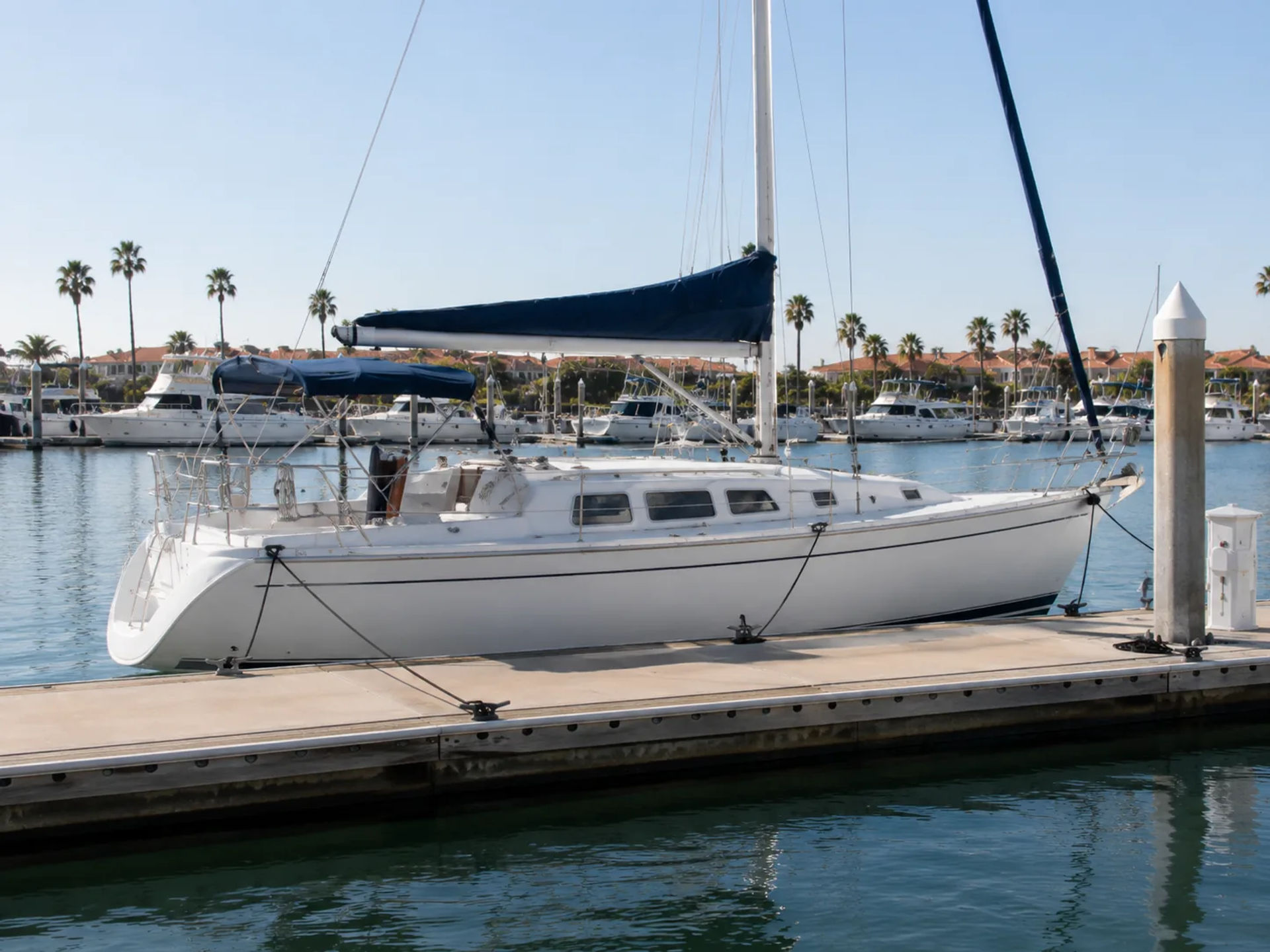 White sailboat tied to a concrete dock with black spring lines