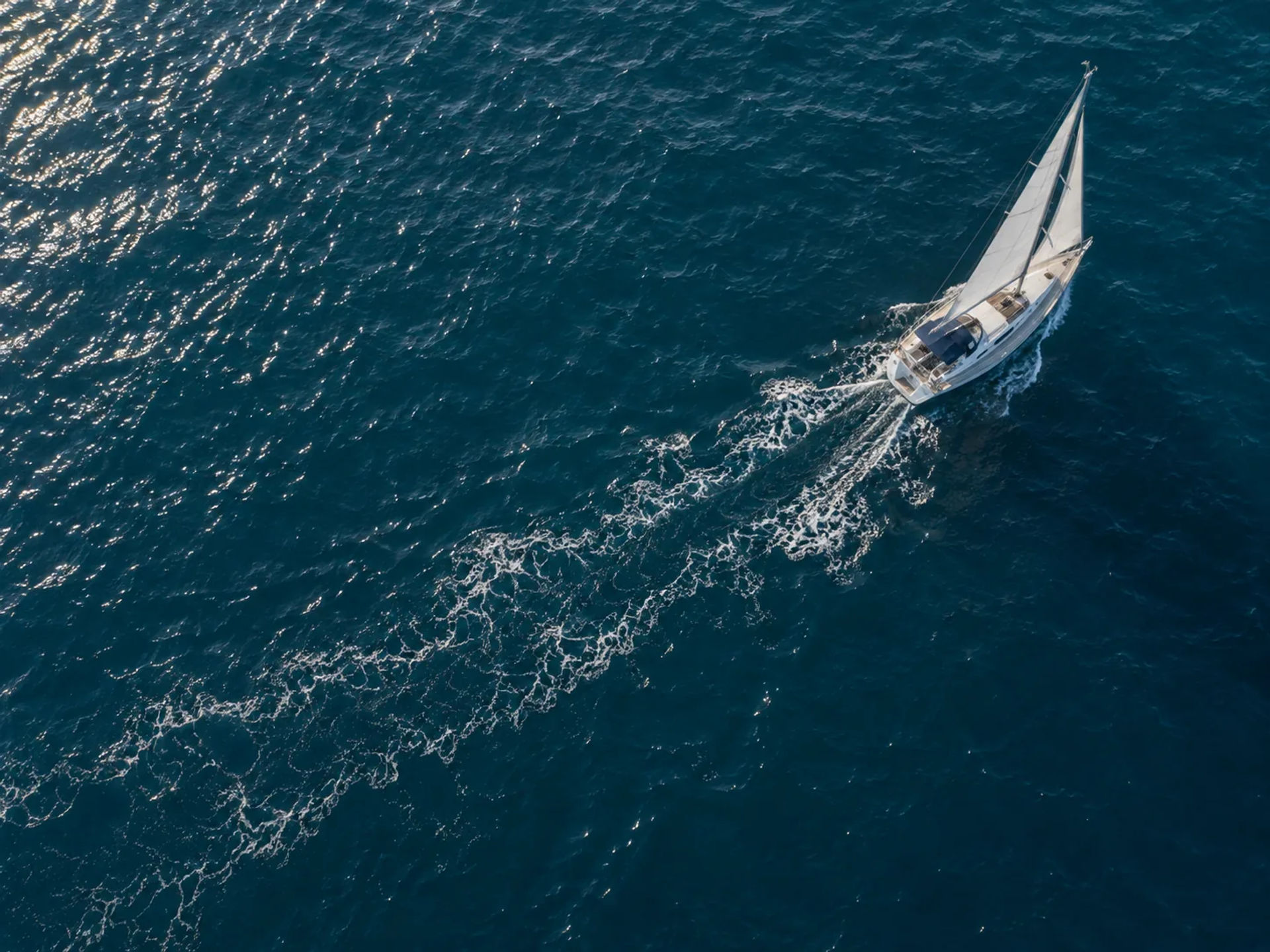 Overhead view of a white sailboat heeling with a foamy V-shaped wake