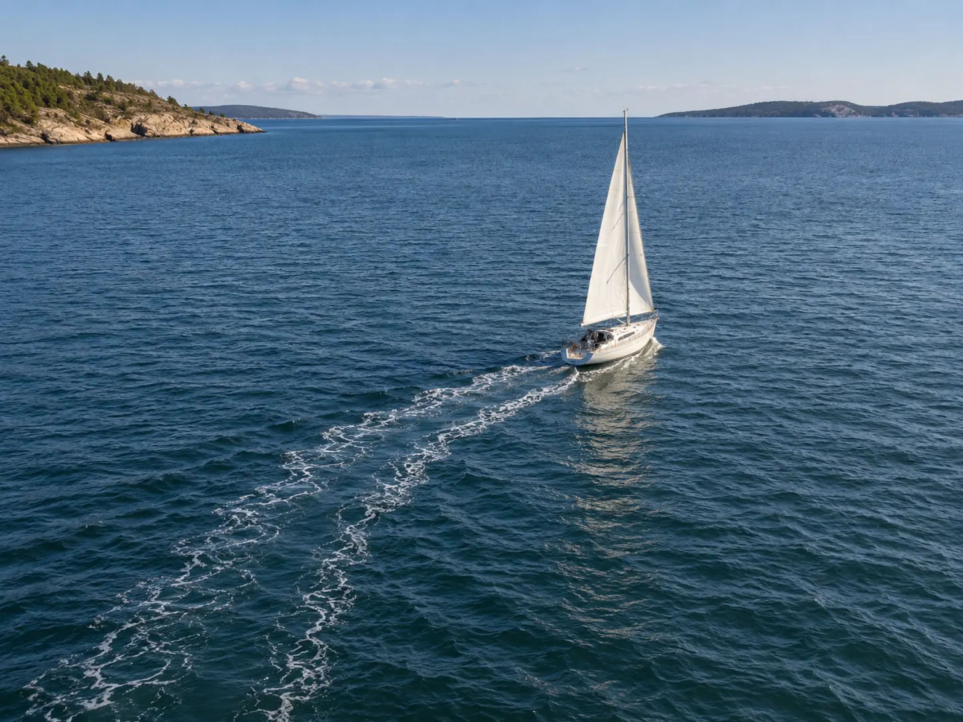 Aerial view of a sailboat with full sails leaving a wake on blue water