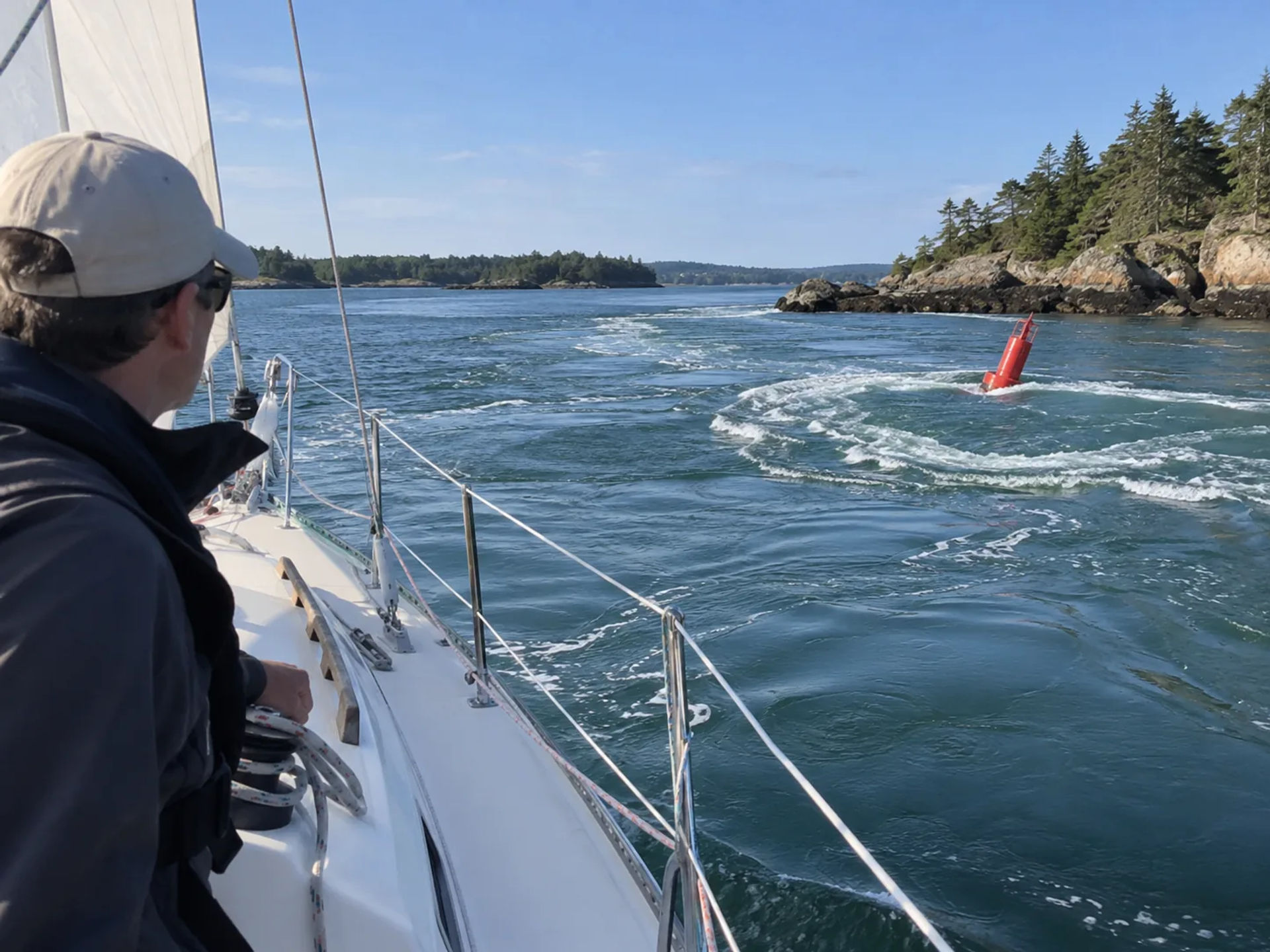 Sailor on deck watching a red buoy leaning in strong turbulent current