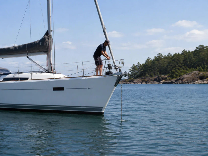 Crew member handling the anchor on the bow of a sailboat