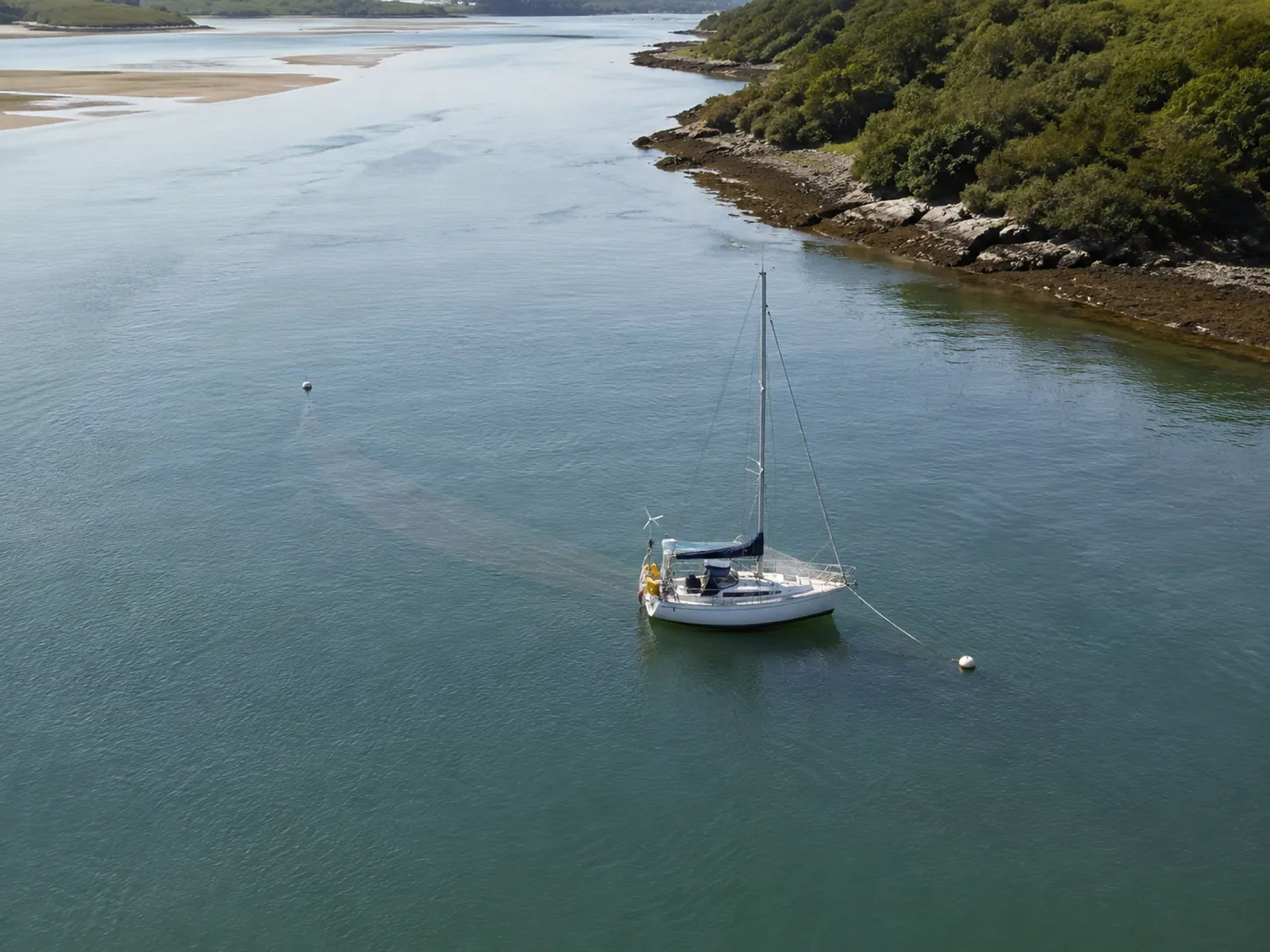 Sailboat moored to a buoy in a sheltered channel with wooded shoreline