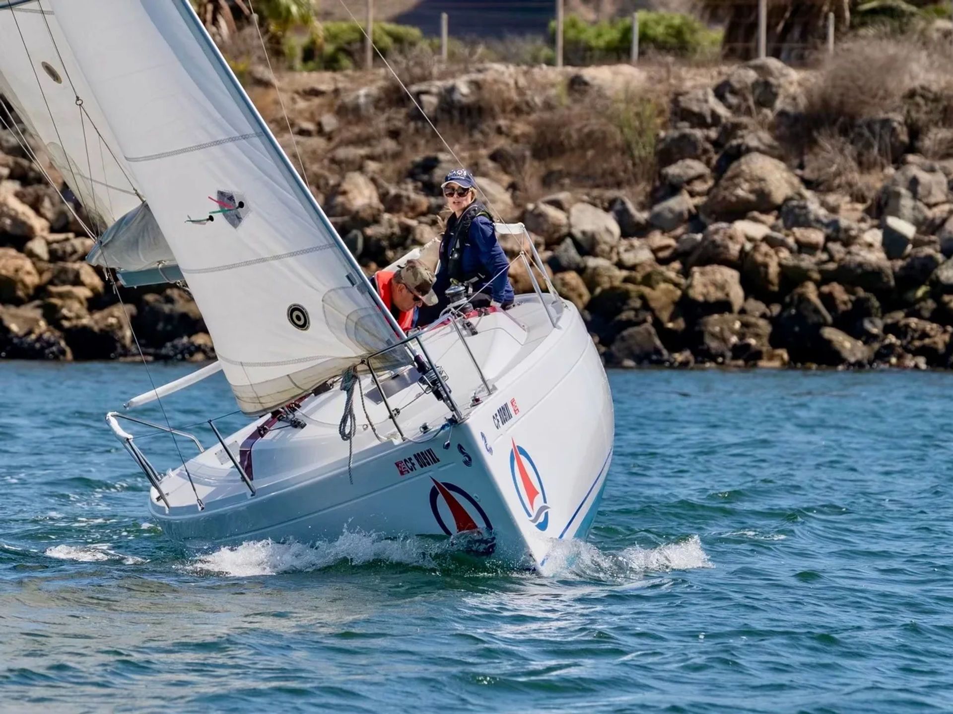 Sailboat sailing along a rocky coastline with full sails