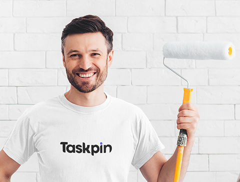 A smiling and ready-to-work master craftsman wearing work clothes and standing next to a blue wall with his hands on his chest