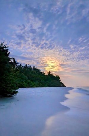 Image étonnante de la plage de Soneva Fushi Maldvies au coucher du soleil avec la lumière dorée et les nuages dans le ciel et réfléchissait sur l'eau côtière.