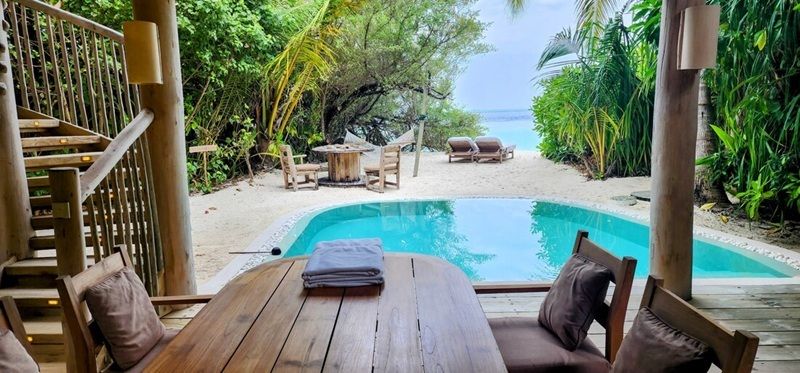 Image de piscine de Sateva Fushi dans les Maldives, entourée de jardins tropicaux verts et de meubles extérieurs extérieurs.