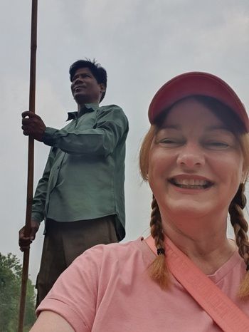Image of travel expert Lisa Thomas smiling while taking a selfie on a canoe ride on the Rapti River in Nepal, with canoe driver behind. 