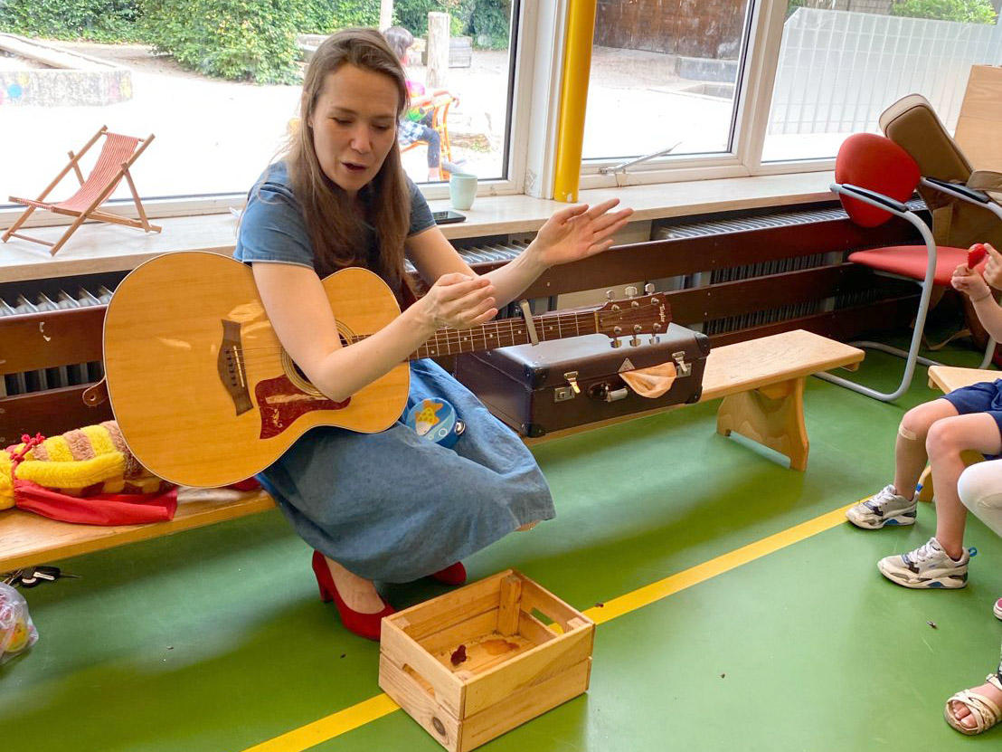 Renee zingt en speelt gitaar voor een groep kinderen tijdens een muziekworkshop in de kinderopvang