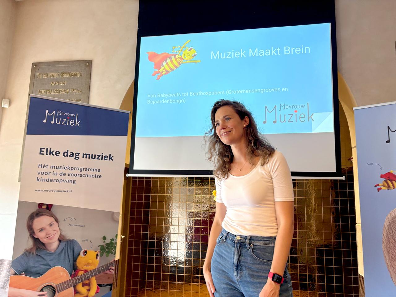 Renee bij een presentatie met de titel 'Muziek maakt brein', naast de banner van Elke dag muziek