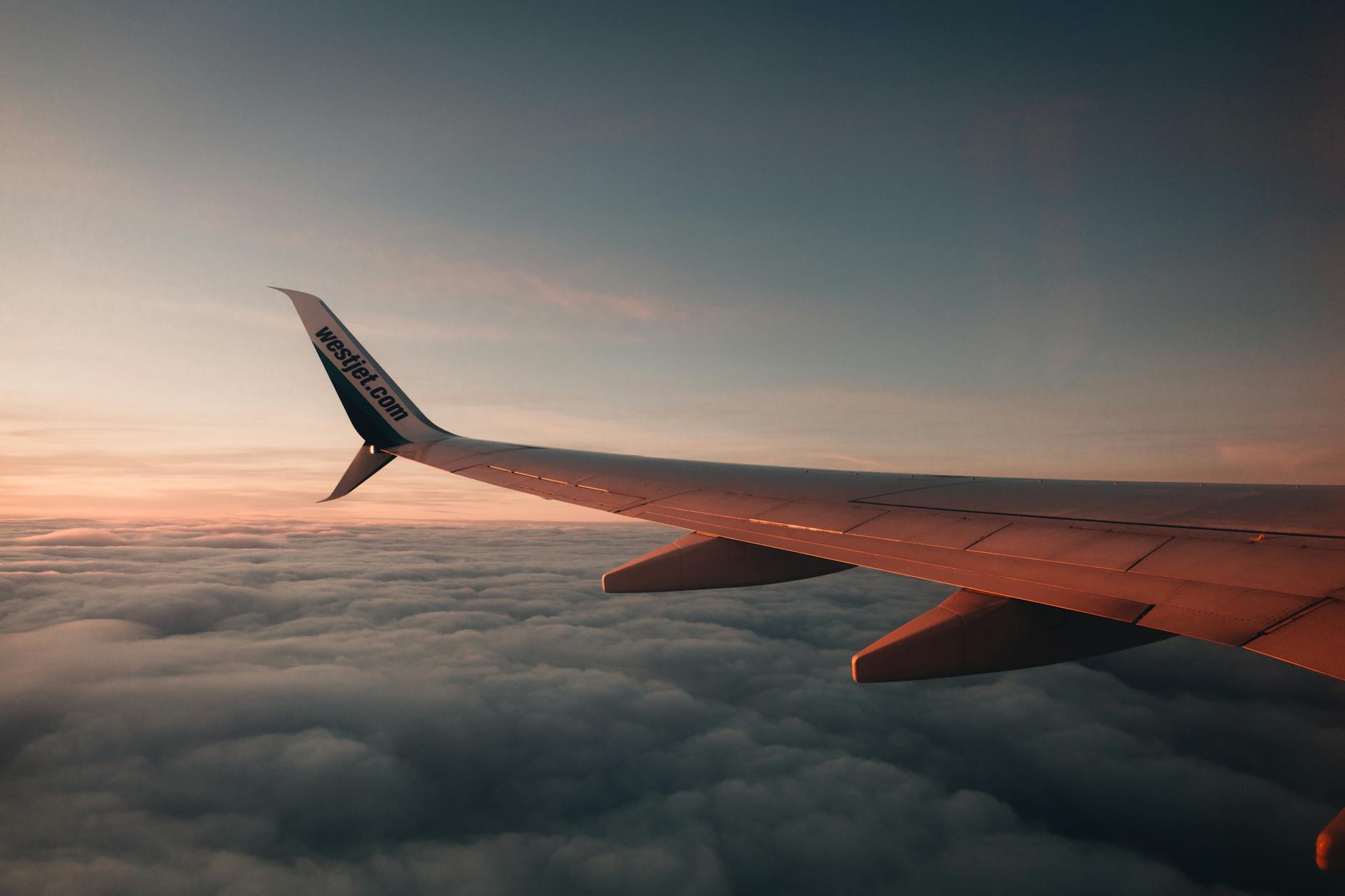 An airplane wing with dramatic lighting flying high over a sea of clouds during twilight.