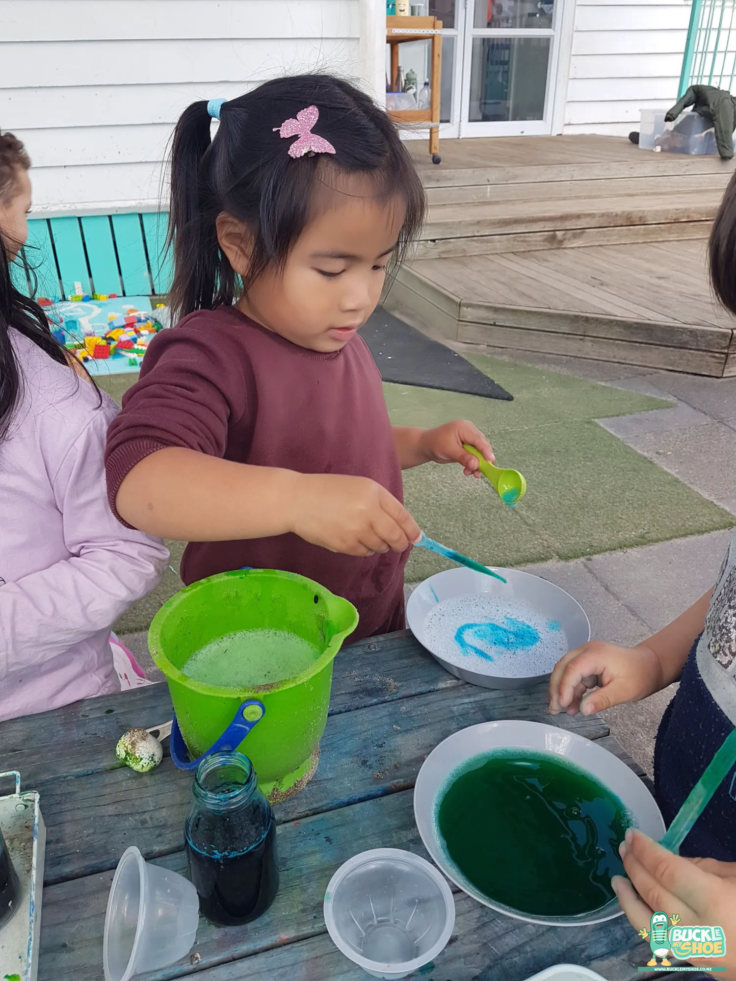 Buckle My Shoe Tauranga & Papamoa | Childcare, Preschool, Daycare | A child smiling while observing their final potion creation in the garden.