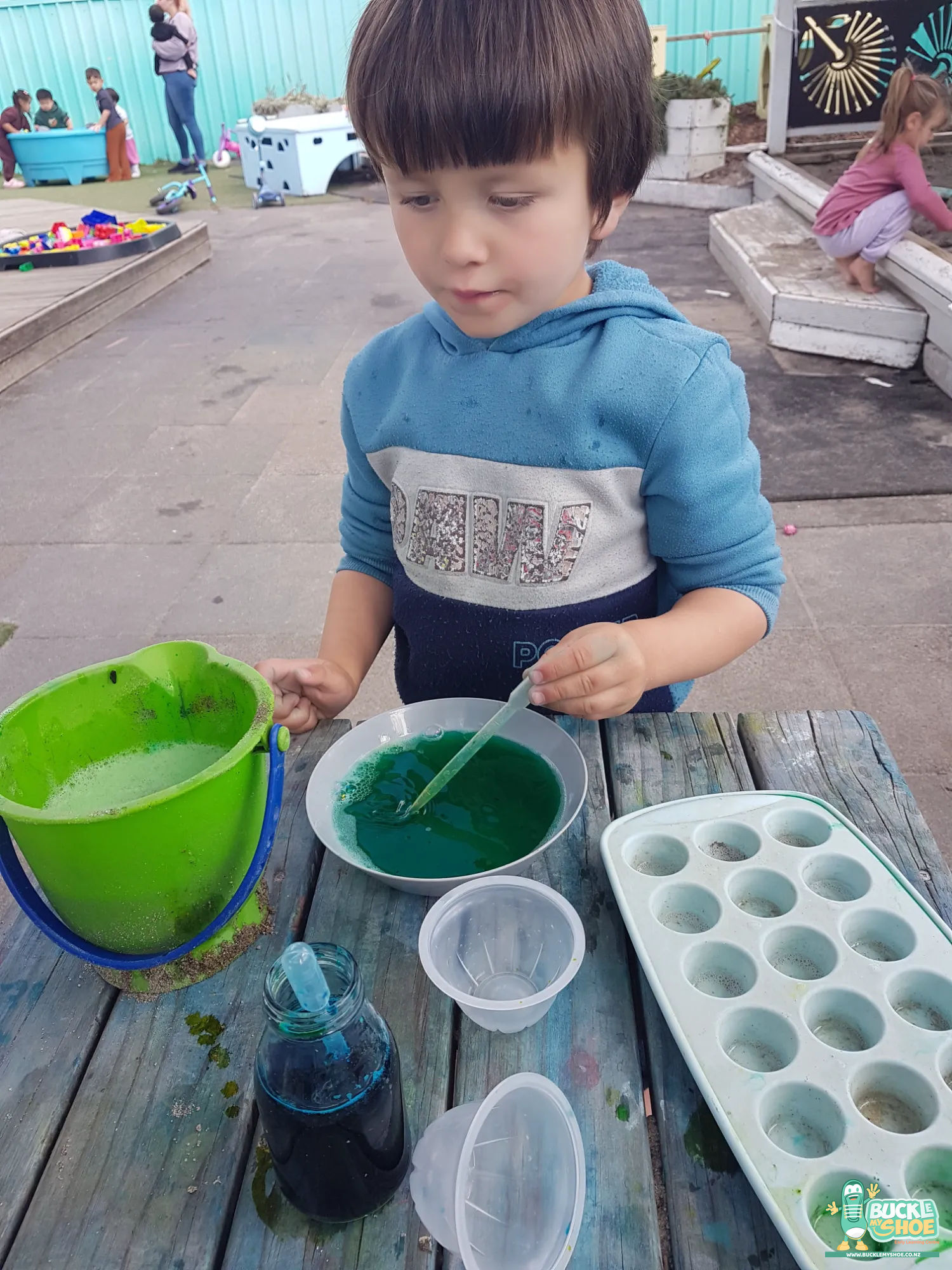 Buckle My Shoe Tauranga & Papamoa | Childcare, Preschool, Daycare | Concentrated tamariki mixing vibrant coloured dyes into containers of clear water.