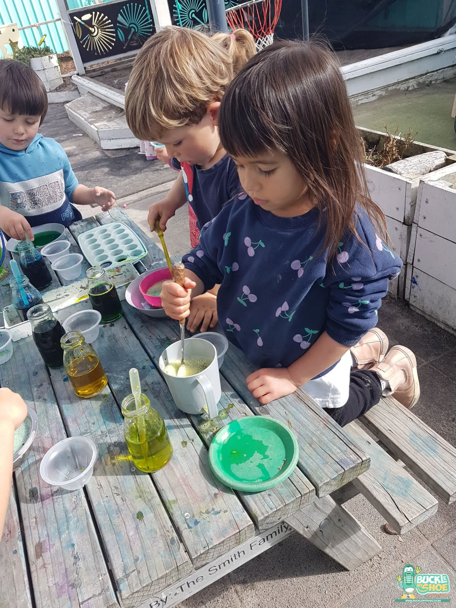 Buckle My Shoe Tauranga & Papamoa | Childcare, Preschool, Daycare | Bright green and blue dye containers waiting on an outdoor wooden table.