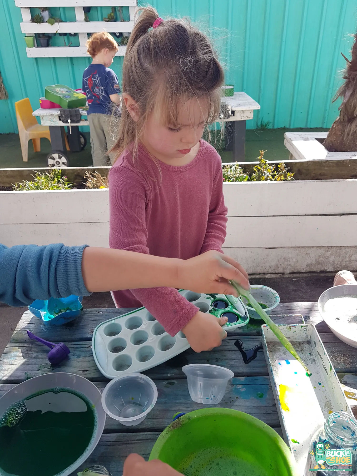Buckle My Shoe Tauranga & Papamoa | Childcare, Preschool, Daycare | A child proudly holding their potion container up against the bright sky.