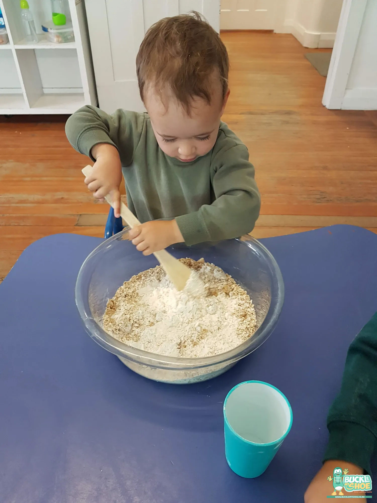 Buckle My Shoe Tauranga & Papamoa | Childcare, Preschool, Daycare | A child holding a wooden spoon up high after stirring the mixture.