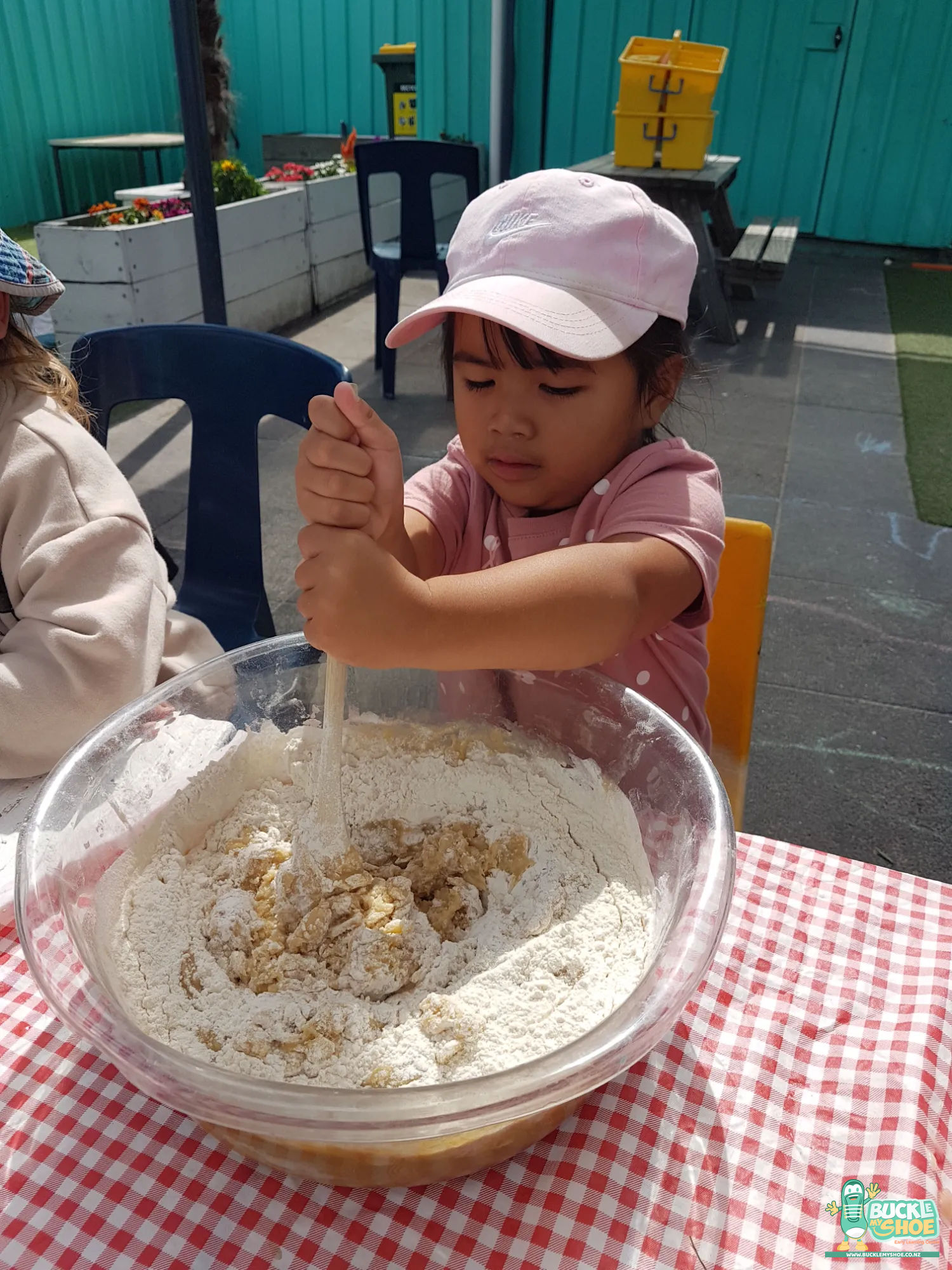Buckle My Shoe Tauranga & Papamoa | Childcare, Preschool, Daycare | A child smiling proudly while using a spoon to scoop cookie dough.