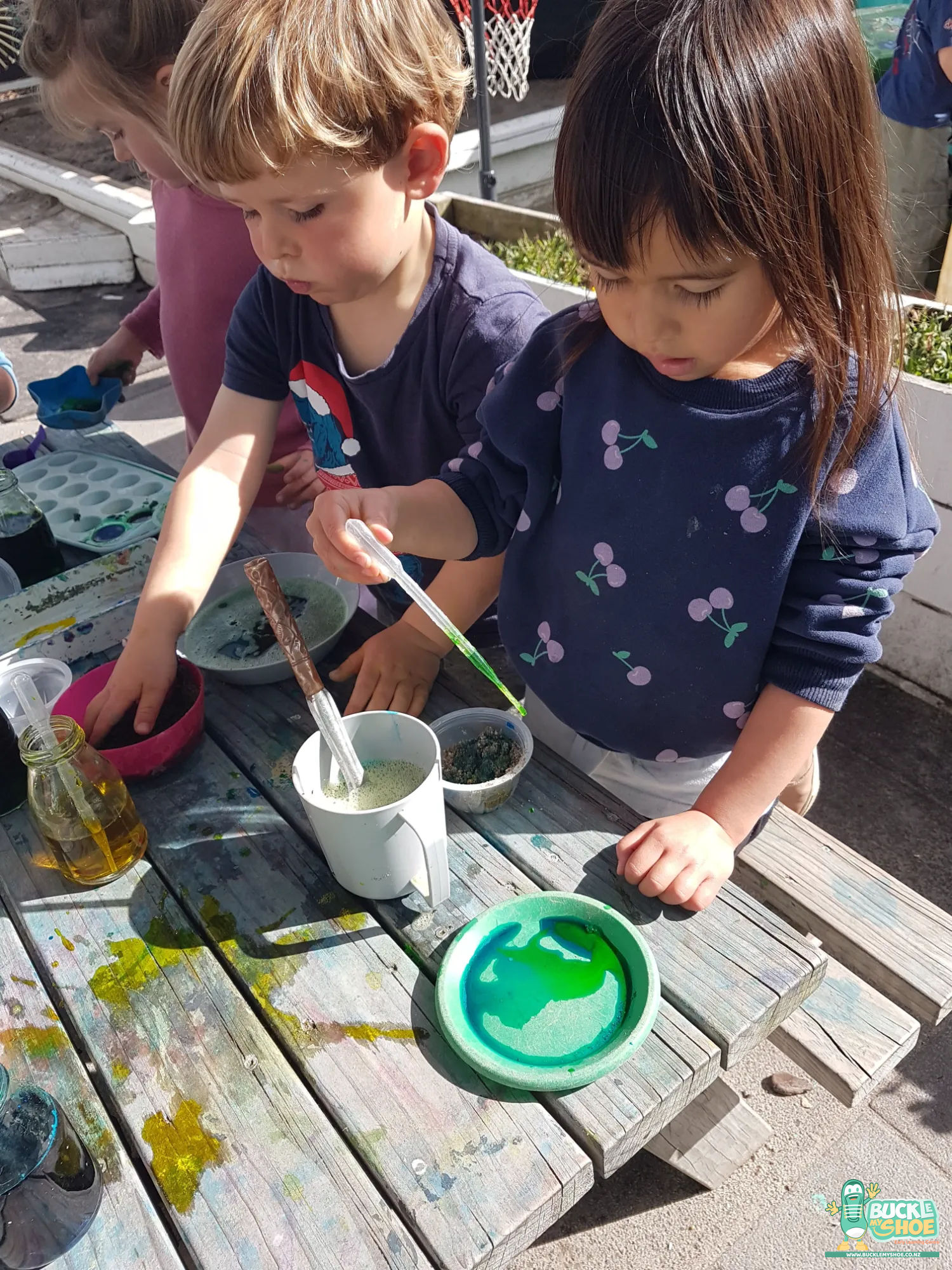 Buckle My Shoe Tauranga & Papamoa | Childcare, Preschool, Daycare | A preschooler carefully stirring sand into their mixture with a plastic spoon.