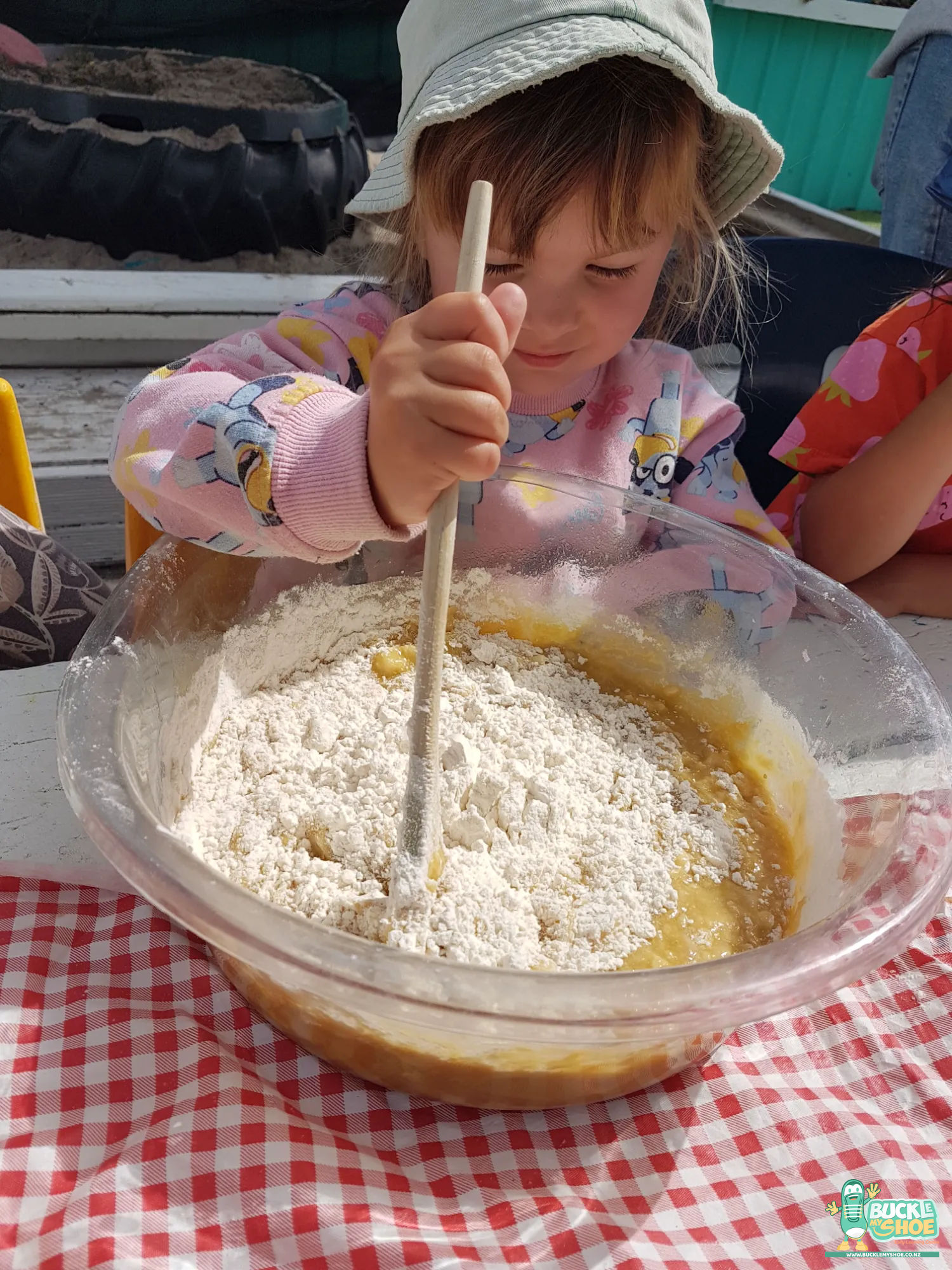 Buckle My Shoe Tauranga & Papamoa | Childcare, Preschool, Daycare | Two children working together to stir a thick batter in a bowl.