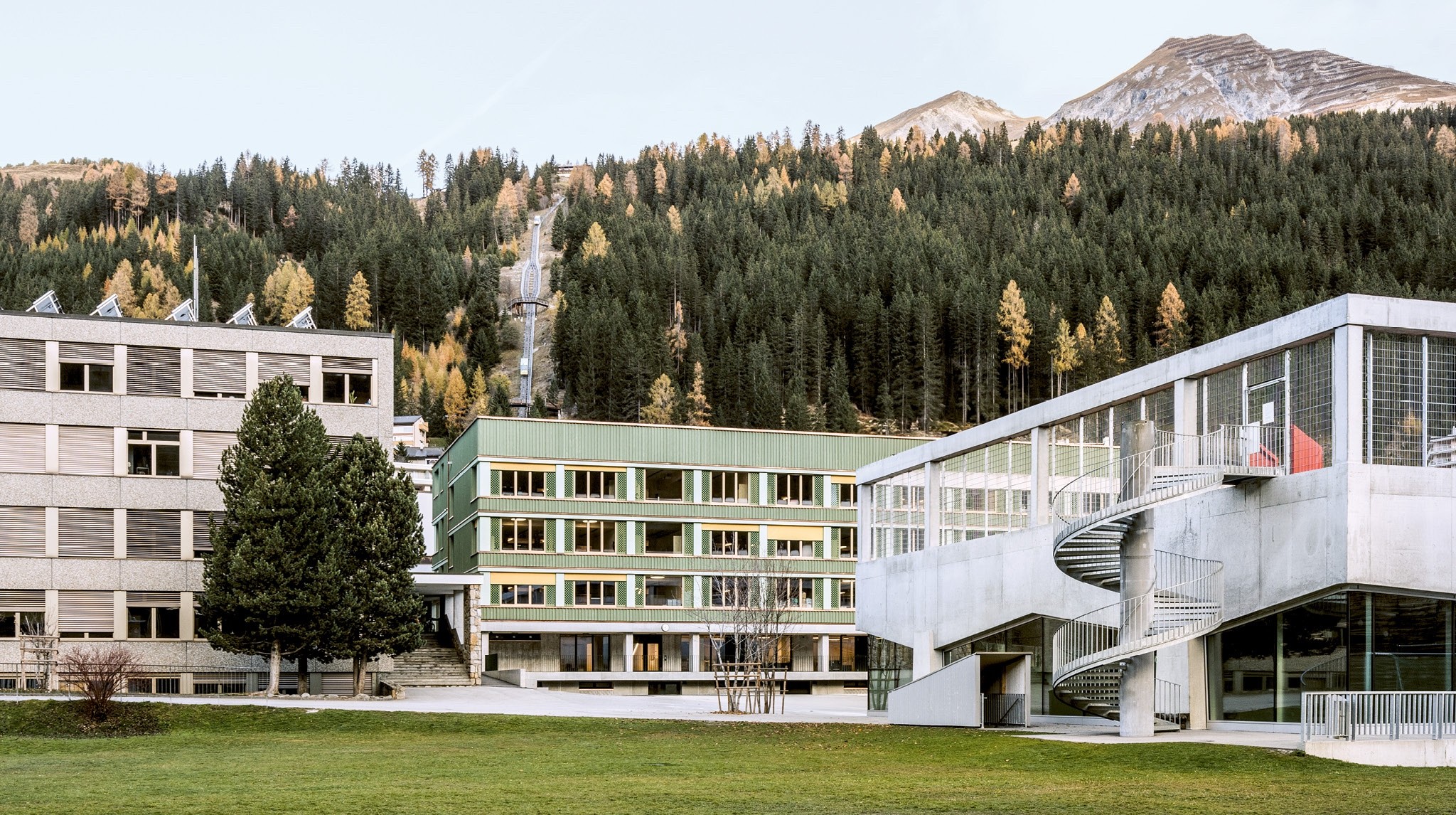Mit heiter hellgrünem Kleid steht die erweiterte Schulanlage in Davos zwischen einem Primar- und Oberschulhaus.