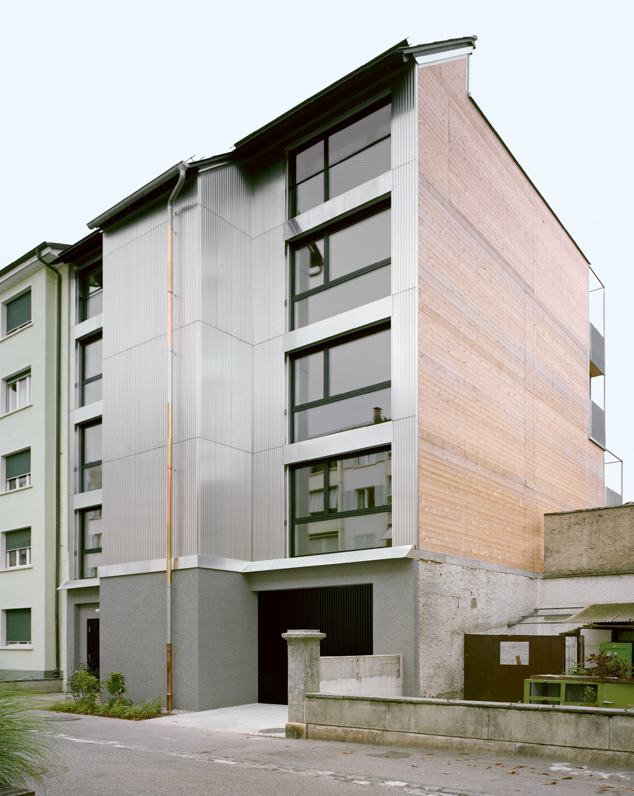 Das Steildach führt die Dachlandschaft des Blockrands weiter. Die Fassade besteht aus rohem Aluminiumblech, das Fallrohr aus Reststücken.