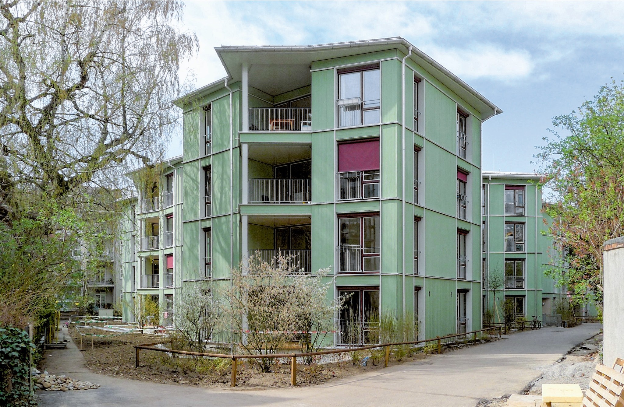 Charakterstarke Fassade: Zwischen Holzlatten in sanftem Hellgrün liegen dunkelrote Stoffmarkisen mit Handkurbeln.