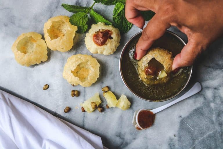 A person stuffing a crispy puri with a flavorful mixture of potatoes, chickpeas, and spices.