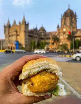 Vada Pav You’ll Regret Not Trying - Best Vada Pav in Mumbai 1 A delicious looking Vada Pav from Aram Vada Pav in a hand with a blurred building in the background